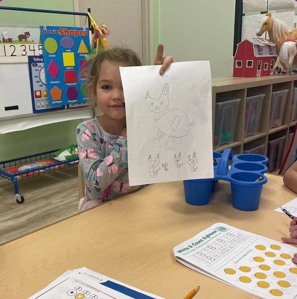 A girl proudly holds up her drawing in class