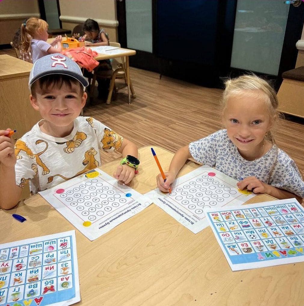 Two smiling preschoolers in paper crowns at a table