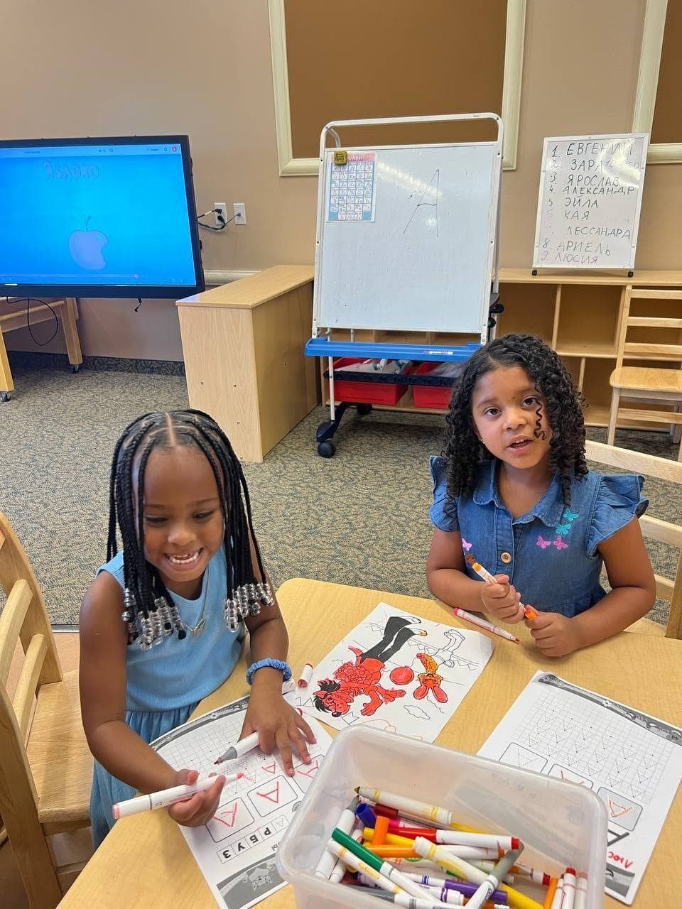 Two smiling girls coloring together at a classroom table