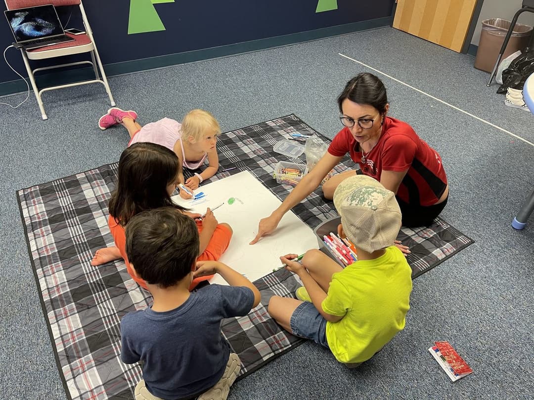 A teacher on the floor with young children on a picnic blanket