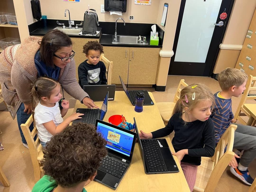 A teacher helps students working on laptops